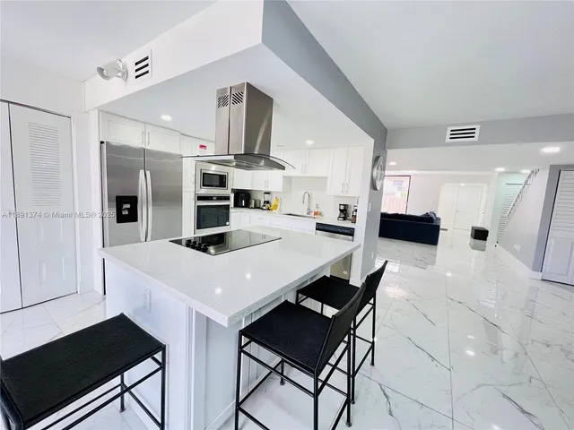 a kitchen with stainless steel appliances kitchen island granite countertop a refrigerator oven a sink dishwasher and white cabinets with wooden floor