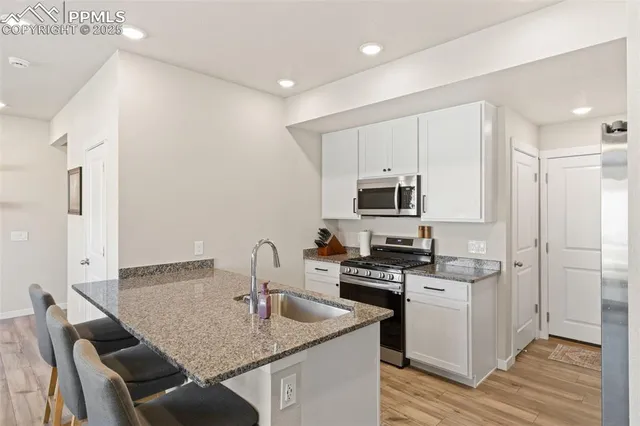 a kitchen with stainless steel appliances granite countertop a stove top oven a sink dishwasher and a refrigerator with wooden floor