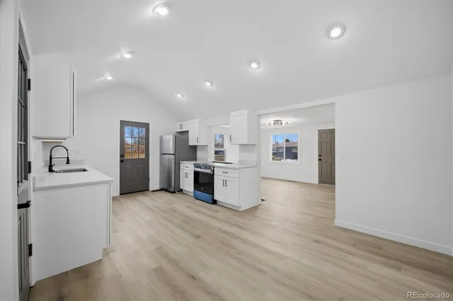 a large kitchen with stainless steel appliances a large counter top a sink dishwasher a refrigerator and a stove with wooden floor