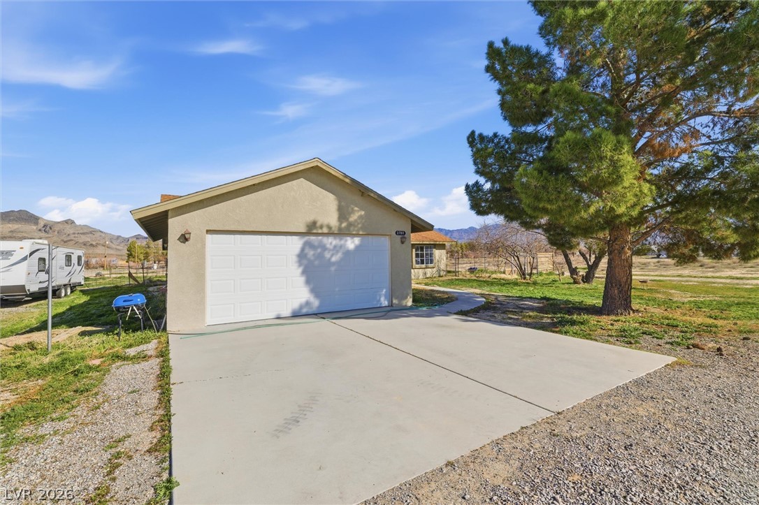 2780 West Simkins Road Pahrump, NV 89060 - Photo 4 of 40 A durable concrete driveway provides easy access to the spacious garage, set against a backdrop of distant mountains and a well-maintained yard.