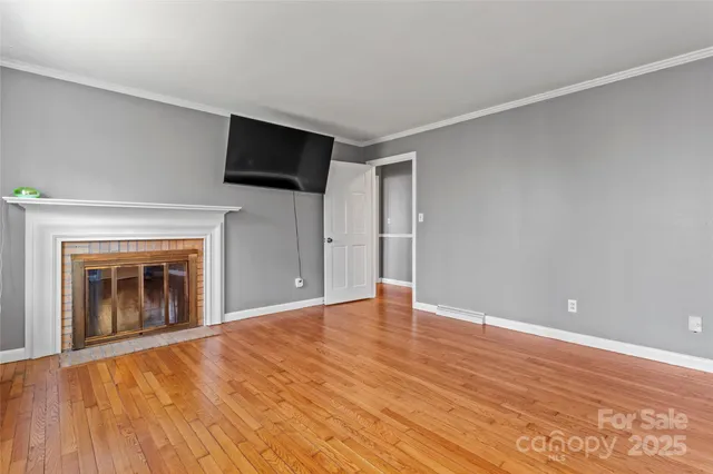 a view of an empty room with wooden floor fireplace and a window