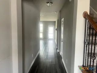 a view of an empty room with wooden floor and a kitchen