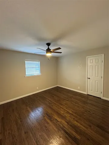 a view of an empty room with wooden floor and a ceiling fan