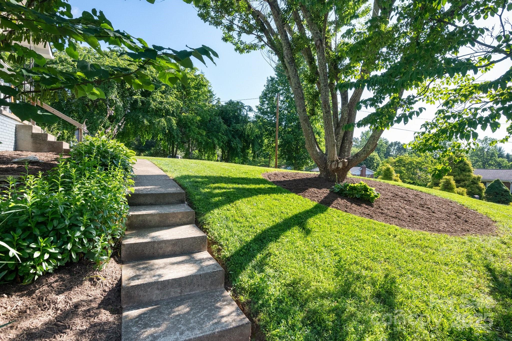 28 Spaulding Road Candler, NC 28715 - Photo 3 of 31 a view of a garden with lawn chairs under an umbrella