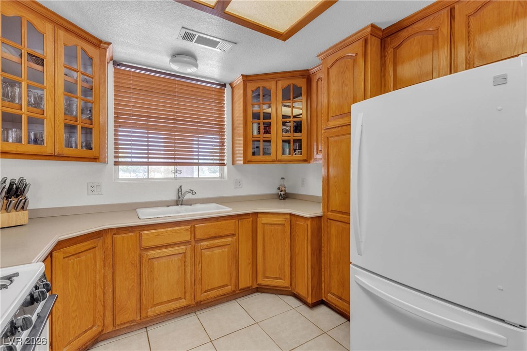 825 West Ryan Avenue Overton, NV 89040 - Photo 26 of 88 Kitchen with freestanding refrigerator, gas range oven, light tile patterned floors, brown cabinets, and glass insert cabinets