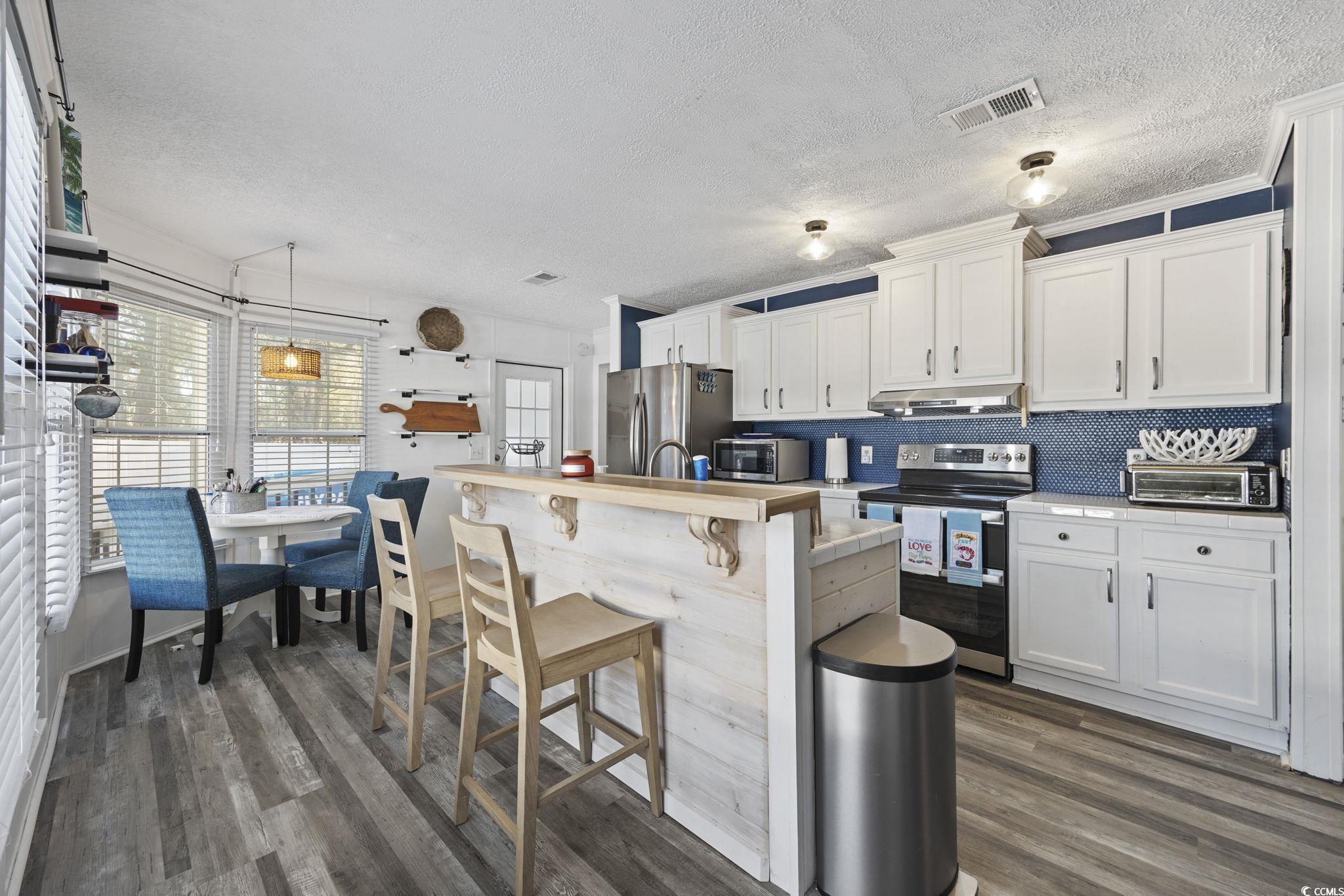 944 Pine Thicket Street Myrtle Beach, SC 29577 - Photo 11 of 27 Kitchen with appliances with stainless steel finishes, a textured ceiling, a kitchen bar, white cabinetry, and dark wood-style floors