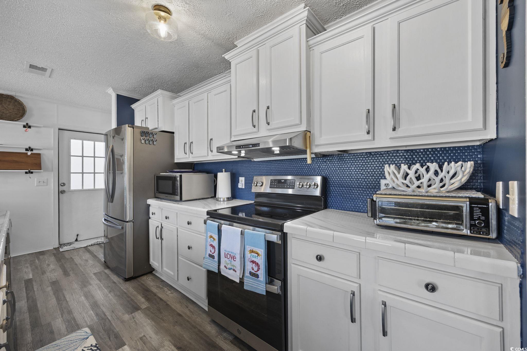 944 Pine Thicket Street Myrtle Beach, SC 29577 - Photo 8 of 27 Kitchen featuring stainless steel appliances, a textured ceiling, white cabinetry, dark wood-type flooring, and under cabinet range hood