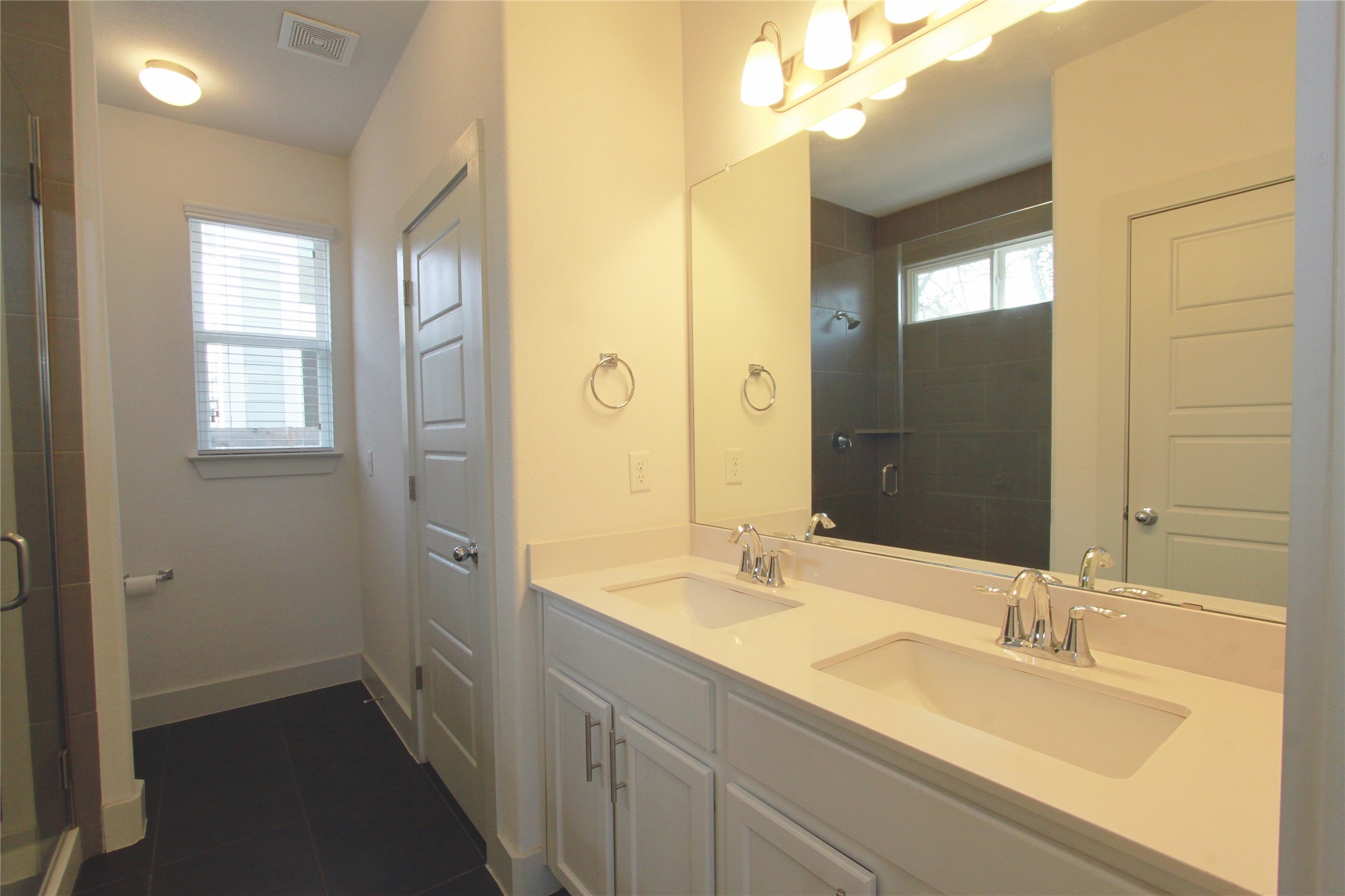 1507 Homespun Road Austin, TX 78745 - Photo 18 of 35 Double vanity with undermount sinks and chrome fixtures, large wall-mounted mirror, white shaker-style cabinetry, and light-toned solid surface countertops