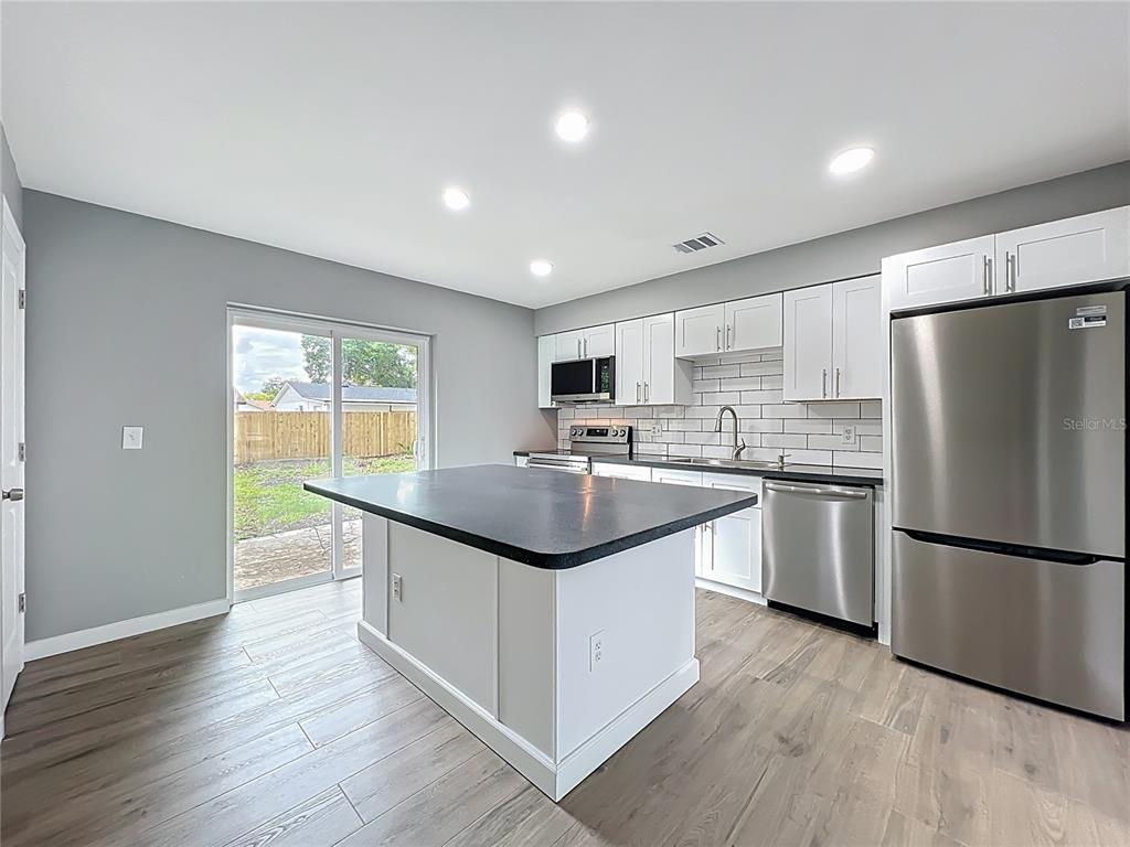 6848 Compass Court Orlando, FL 32810 - Photo 13 of 47 a kitchen with stainless steel appliances granite countertop a refrigerator a sink dishwasher a stove with white cabinets and wooden floor