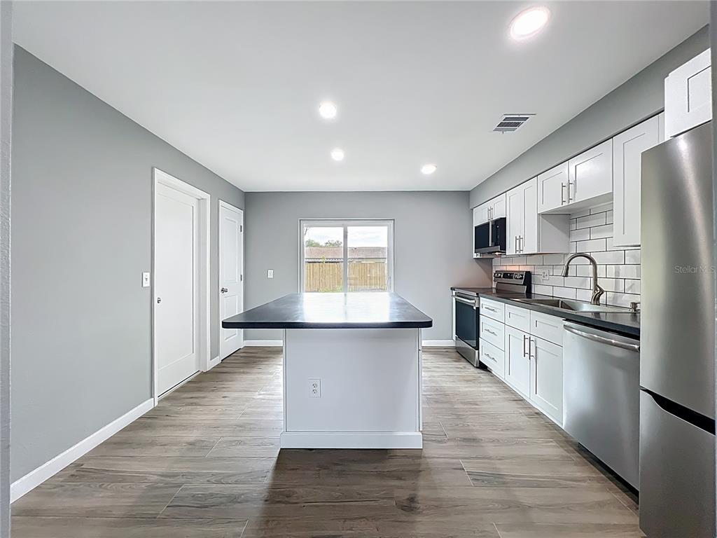 6848 Compass Court Orlando, FL 32810 - Photo 14 of 47 a large kitchen with stainless steel appliances granite countertop a stove a sink dishwasher and a refrigerator with wooden floor