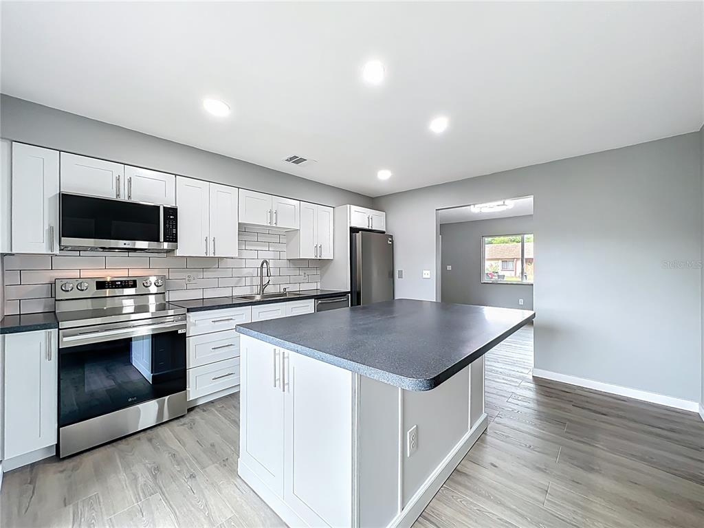 6848 Compass Court Orlando, FL 32810 - Photo 2 of 47 a kitchen with stainless steel appliances kitchen island granite countertop a stove a sink and a microwave