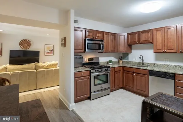 a kitchen with stainless steel appliances granite countertop a stove top oven a sink dishwasher and a refrigerator with wooden floor