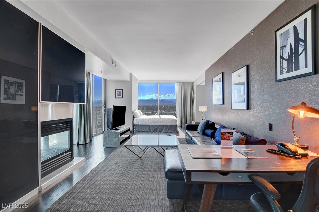 4381 West Flamingo Road, Unit 1121 Las Vegas, NV 89103 - Photo 7 of 33 Living room featuring wood finished floors, a wall of windows, a textured wall, and a multi sided fireplace