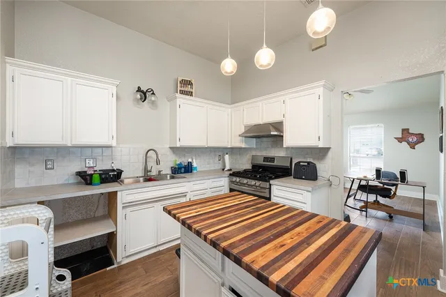a kitchen with sink stove and white cabinets with wooden floor