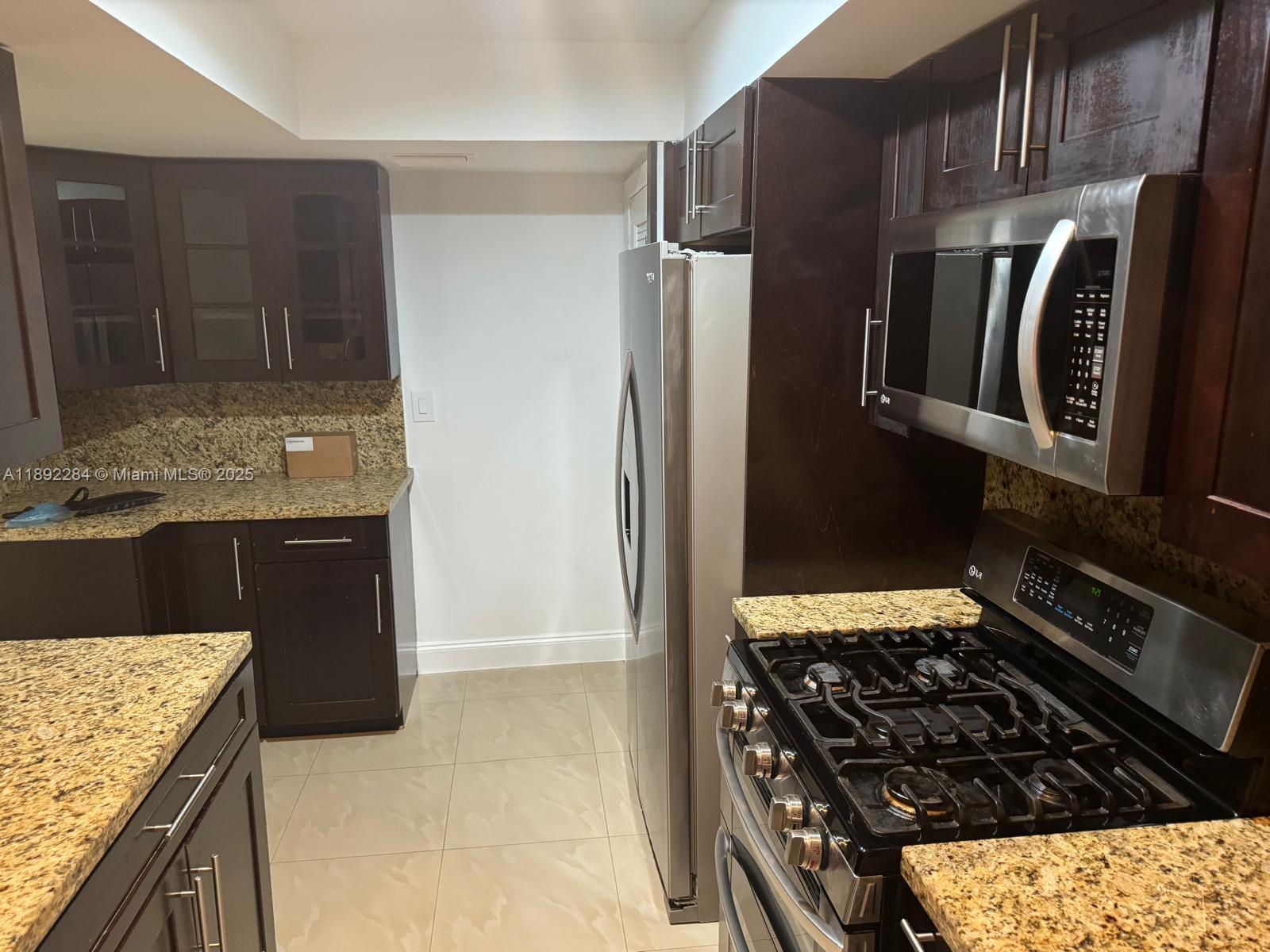 18101 Northwest 68th Avenue, Unit D207 Hialeah, FL 33015 - Photo 7 of 18 a kitchen with granite countertop a refrigerator and a stove