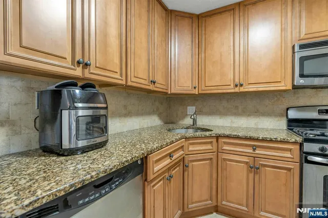 a kitchen with granite countertop stainless steel appliances a sink a stove and cabinets