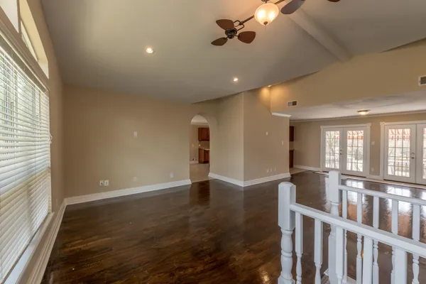 an empty room with wooden floor chandelier fan and windows