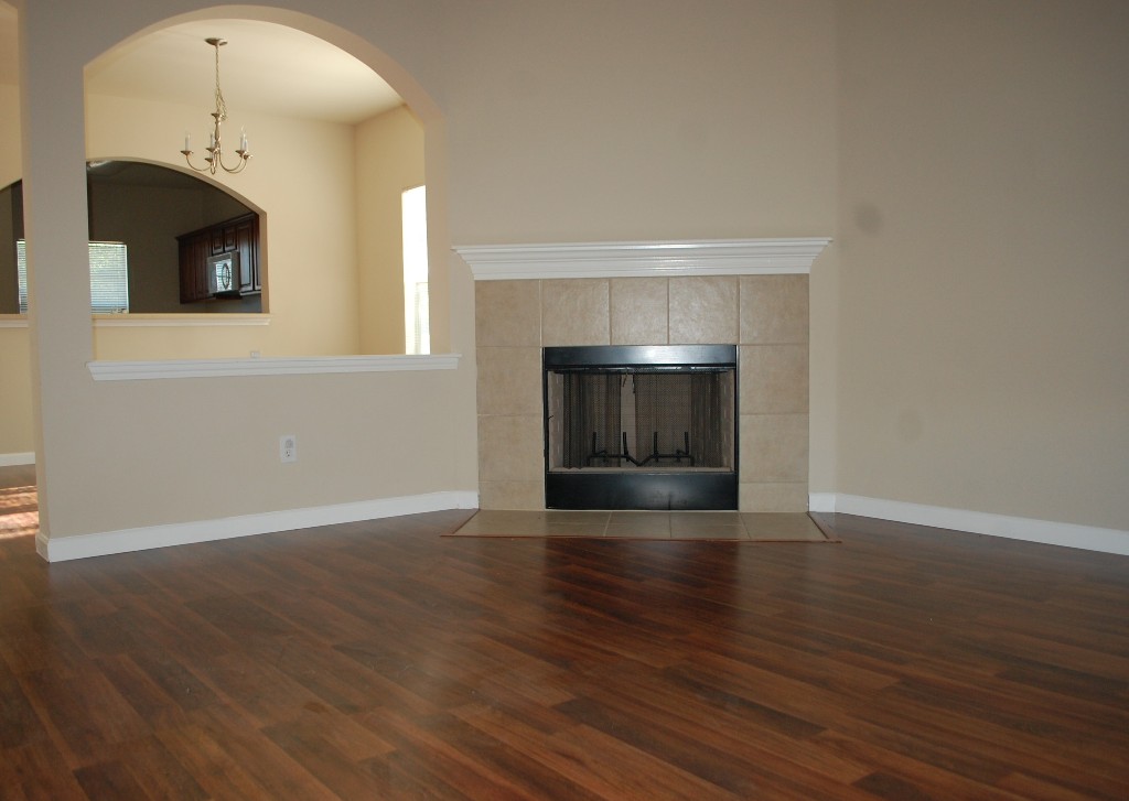 11300 Dimmit Street Manor, TX 78653 - Photo 10 of 23 Hardwood flooring gleams under the archway, leading to a fireplace with tile surround.