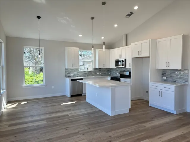 a kitchen with granite countertop a stove a sink dishwasher a refrigerator and white cabinets with wooden floor