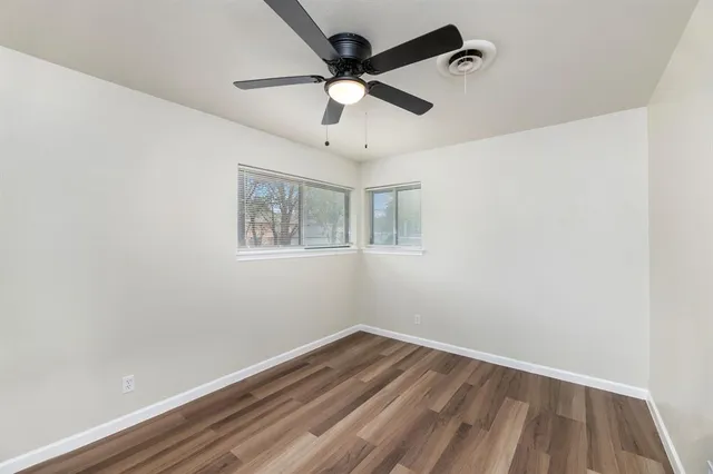 an empty room with wooden floor ceiling fan and windows