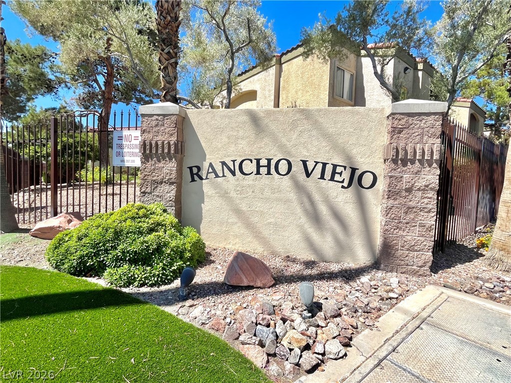 7885 West Flamingo Road, Unit 1029 Las Vegas, NV 89147 - Photo 1 of 18 A welcoming entrance to the community of Rancho Viejo, featuring a stone wall, lush greenery, and secure fencing.