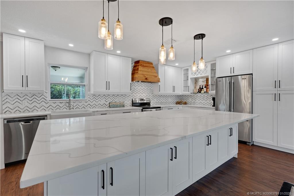 2916 Southeast Paramount Place Stuart, FL 34997 - Photo 2 of 38 a kitchen with stainless steel appliances kitchen island granite countertop a sink a microwave a refrigerator and white cabinets