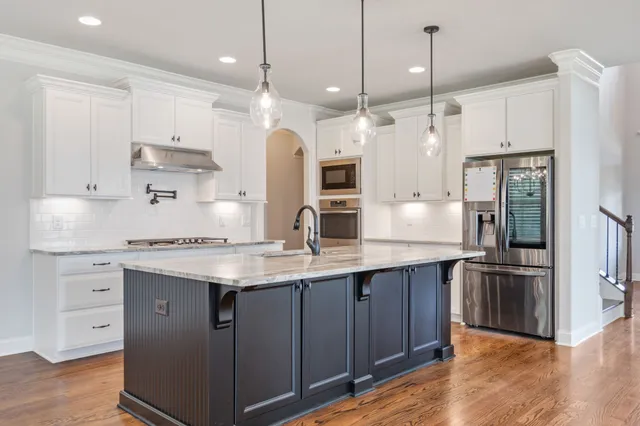 a kitchen with stainless steel appliances kitchen island granite countertop a stove top oven a sink a refrigerator and white cabinets with wooden floor