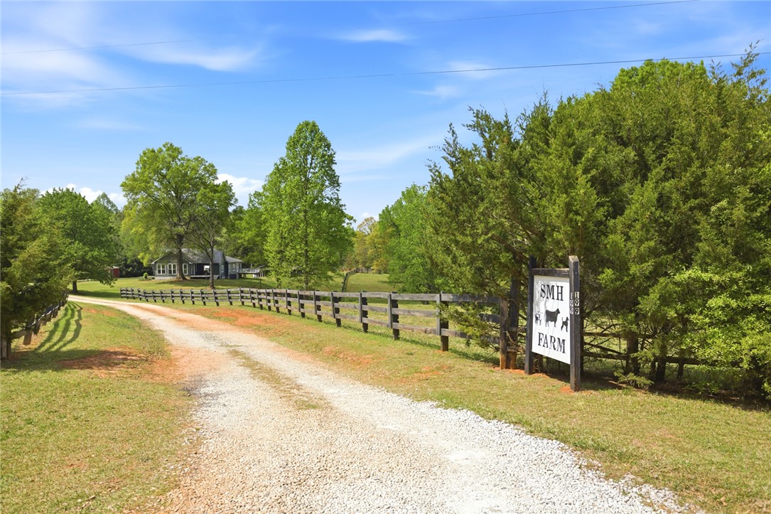 199 Williams Farm Road Westminster, SC 29693 - Photo 41 of 47 A picturesque gravel driveway leads to a secluded farm house, surrounded by lush greenery and a classic wooden fence.