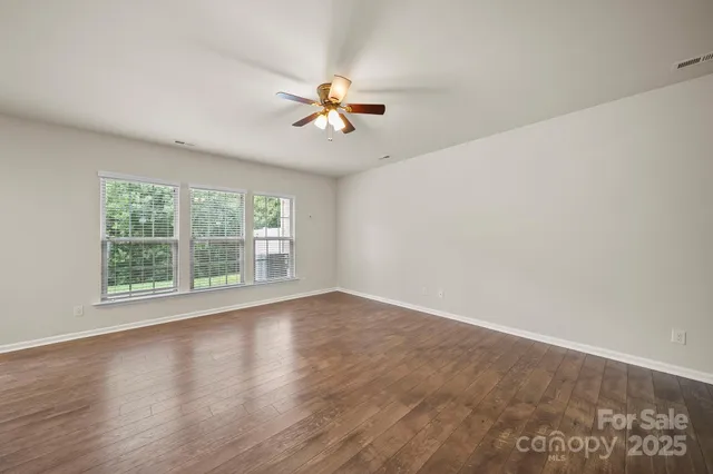 an empty room with wooden floor fan and windows