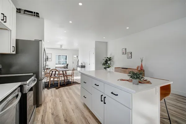 a kitchen with granite countertop a refrigerator a sink a stove and white cabinets with wooden floor