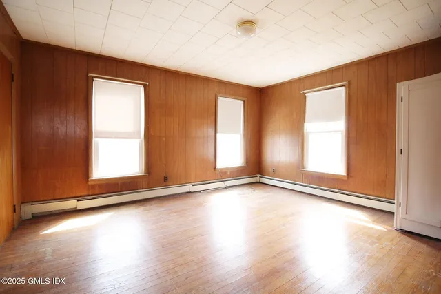 an empty room with wooden floor and windows with curtains