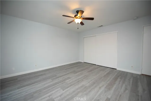 a view of an empty room with wooden floor and a ceiling fan