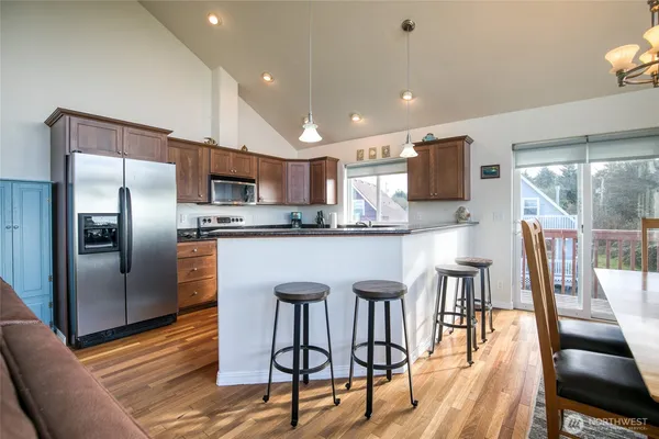 a kitchen with stainless steel appliances granite countertop a refrigerator a stove a sink a dining table and chairs with wooden floor