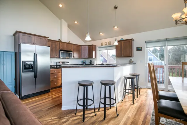 a kitchen with stainless steel appliances granite countertop a refrigerator a stove a sink a dining table and chairs with wooden floor