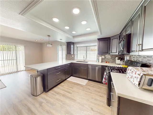 a kitchen with stainless steel appliances kitchen island granite countertop a refrigerator a sink dishwasher a stove with wooden cabinets and floor