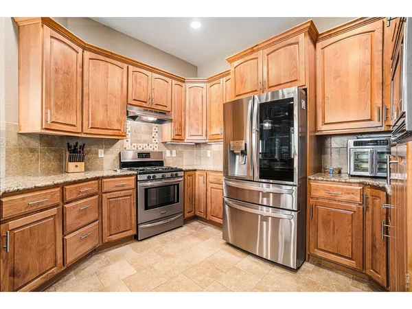 a kitchen with stainless steel appliances granite countertop a refrigerator a stove and a sink with cabinets