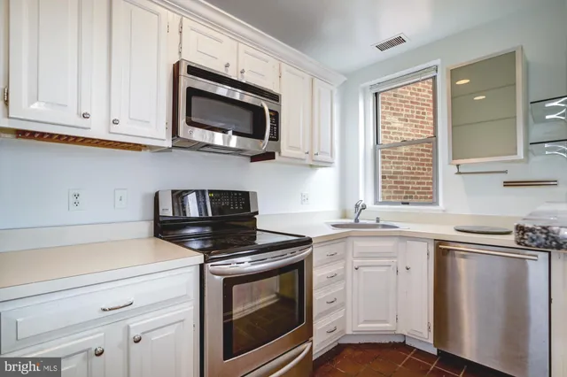 a kitchen with stainless steel appliances granite countertop grey cabinets a stove a sink and a window