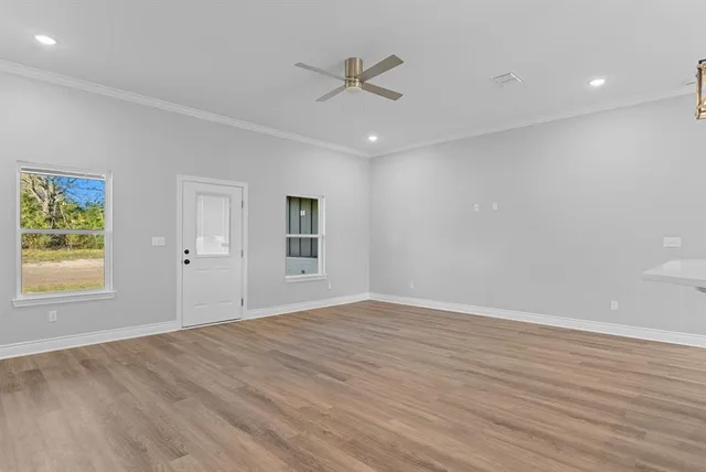 an empty room with wooden floor ceiling fan and windows