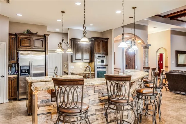 a kitchen with stainless steel appliances kitchen island granite countertop a dining table chairs and a refrigerator