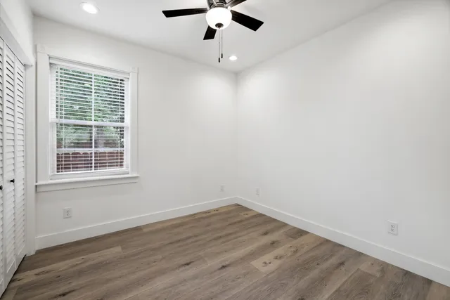 an empty room with wooden floor ceiling fan and window