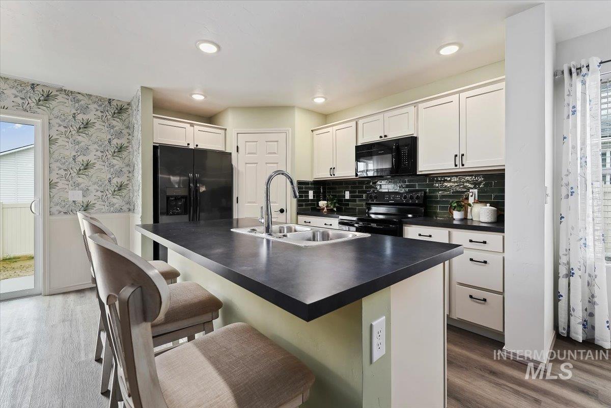 12781 Ashfield Street Caldwell, ID 83607 - Photo 13 of 36 Kitchen with dark countertops, white cabinets, black appliances, an island with sink, and a wainscoted wall