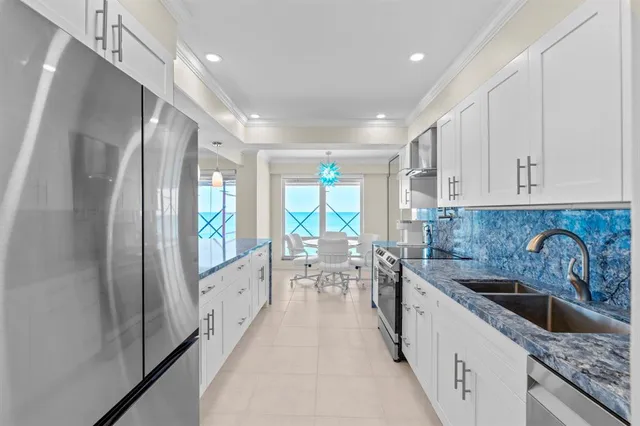a large white kitchen with lots of counter space a sink a refrigerator and a large window