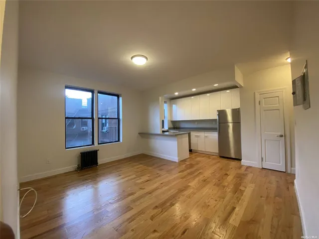 a view of an empty room with wooden floor and a kitchen