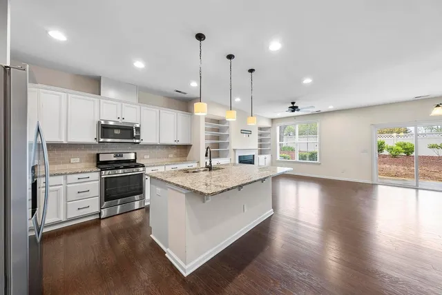 a kitchen with stainless steel appliances granite countertop a stove top oven a sink dishwasher a refrigerator and a dining table with wooden floor