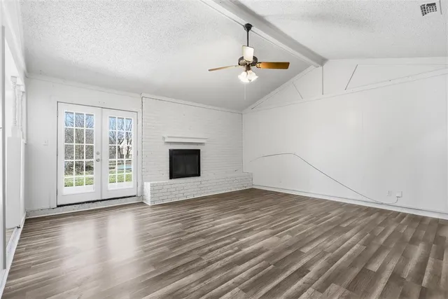 an empty room with wooden floor chandelier and windows