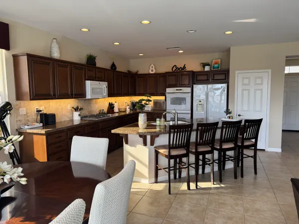 a kitchen with stainless steel appliances kitchen island granite countertop a dining table chairs and a refrigerator
