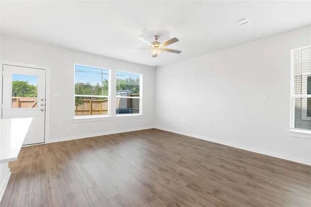 an empty room with wooden floor chandelier fan and windows