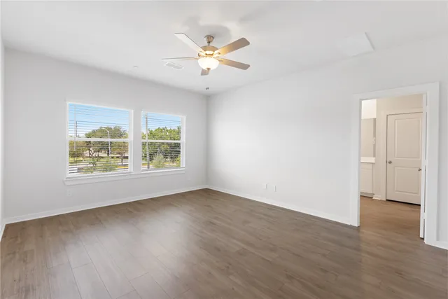 an empty room with wooden floor chandelier fan and windows