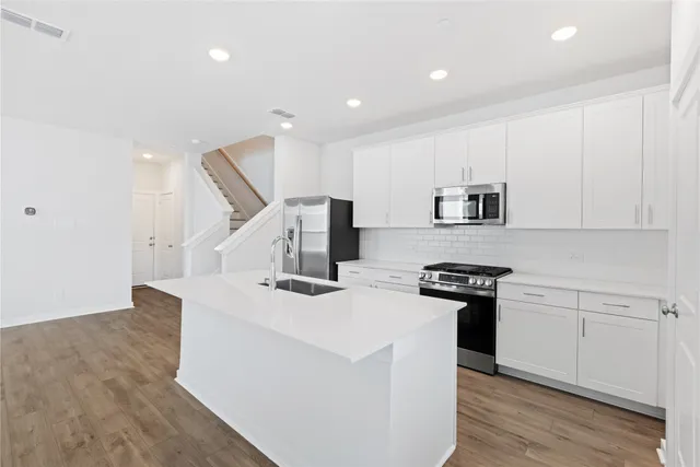 a kitchen with stainless steel appliances kitchen island a stove a sink a refrigerator and white cabinets