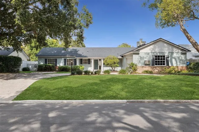 a view of house in front of a big yard with large trees